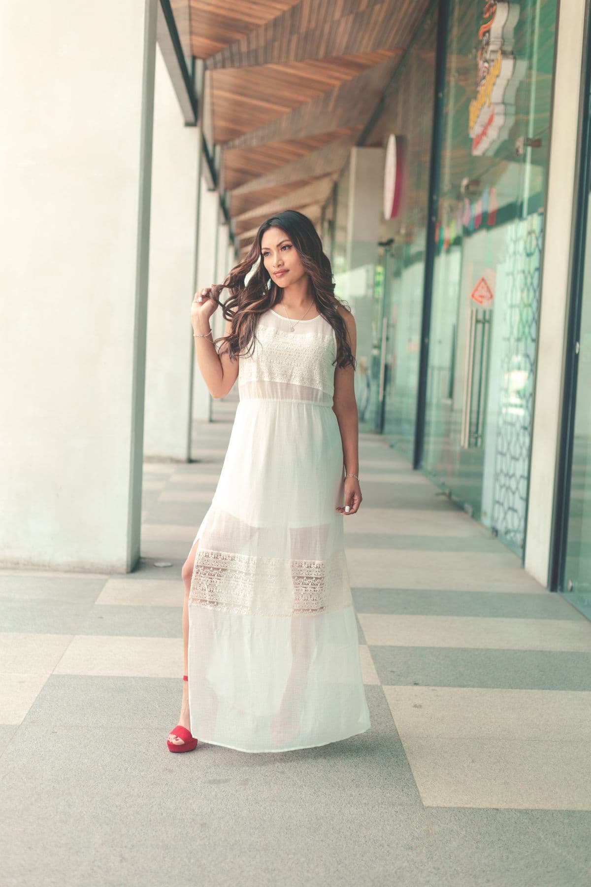 Woman in a flowing white dress walking through a sunlit architectural corridor