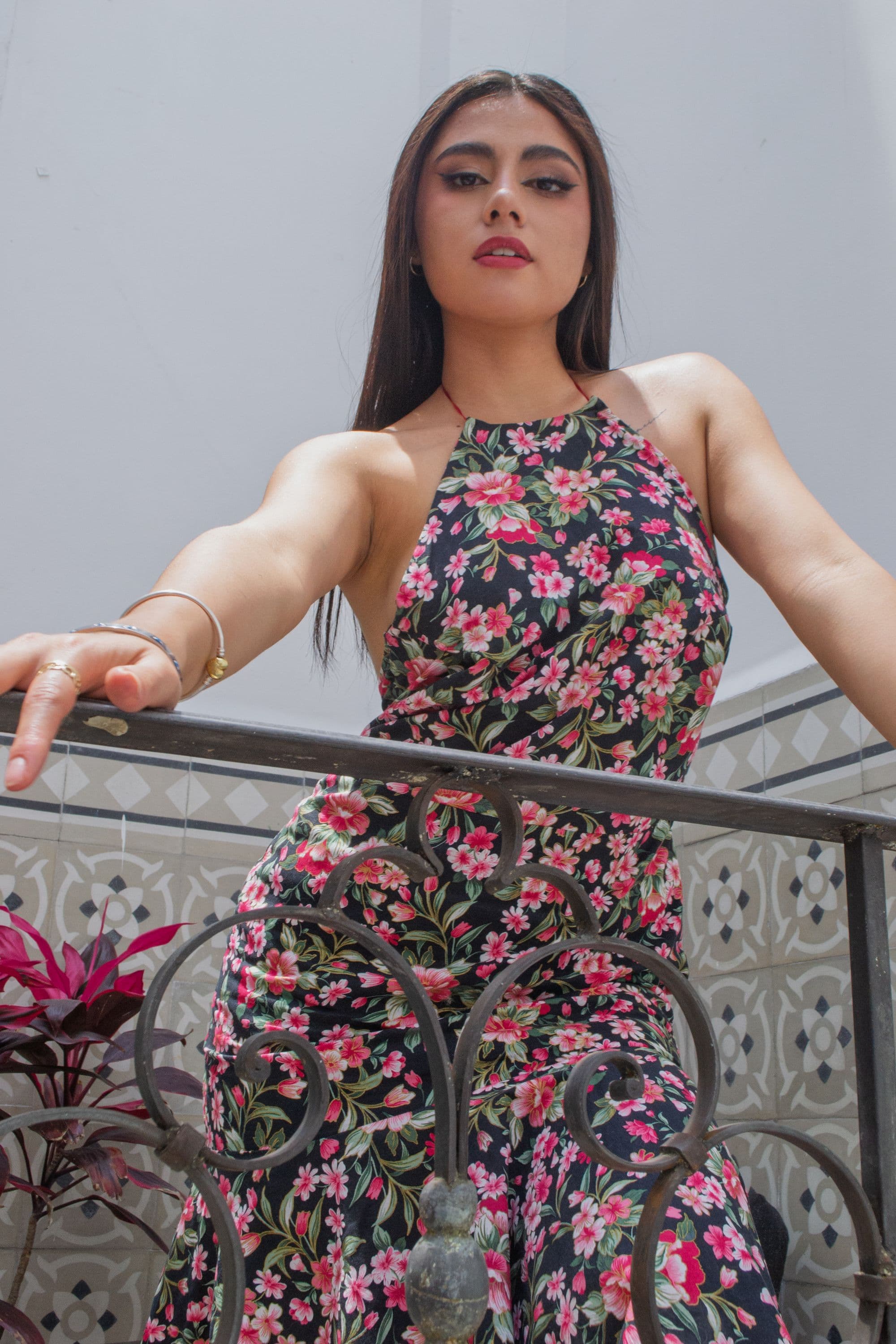 Elegant woman in a floral print dress on a Mediterranean balcony, warm natural light